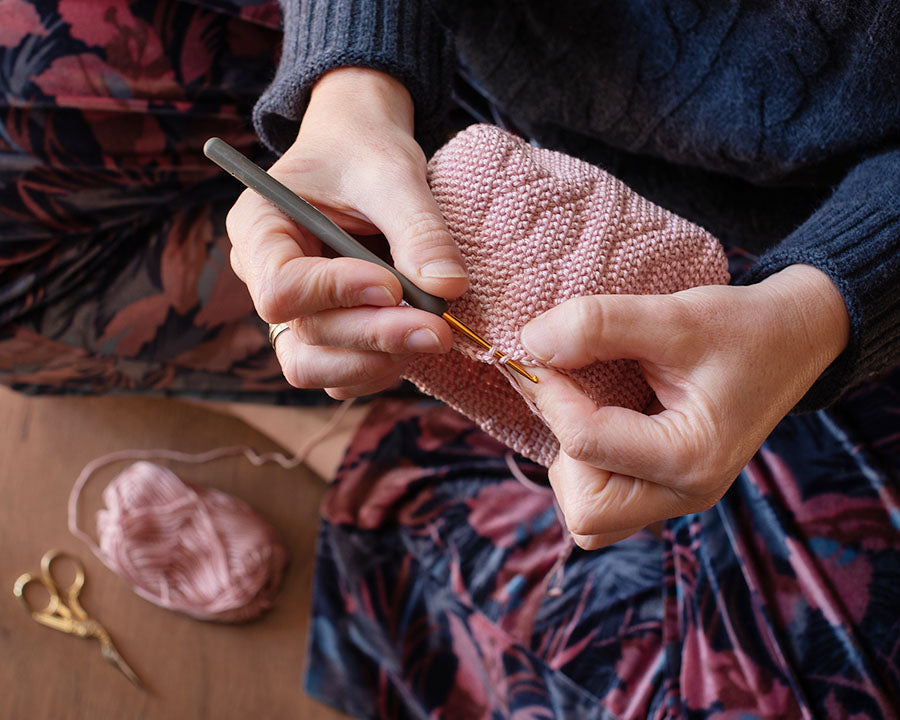 manos tejiendo un patrón de crochet de un monedero color rosa