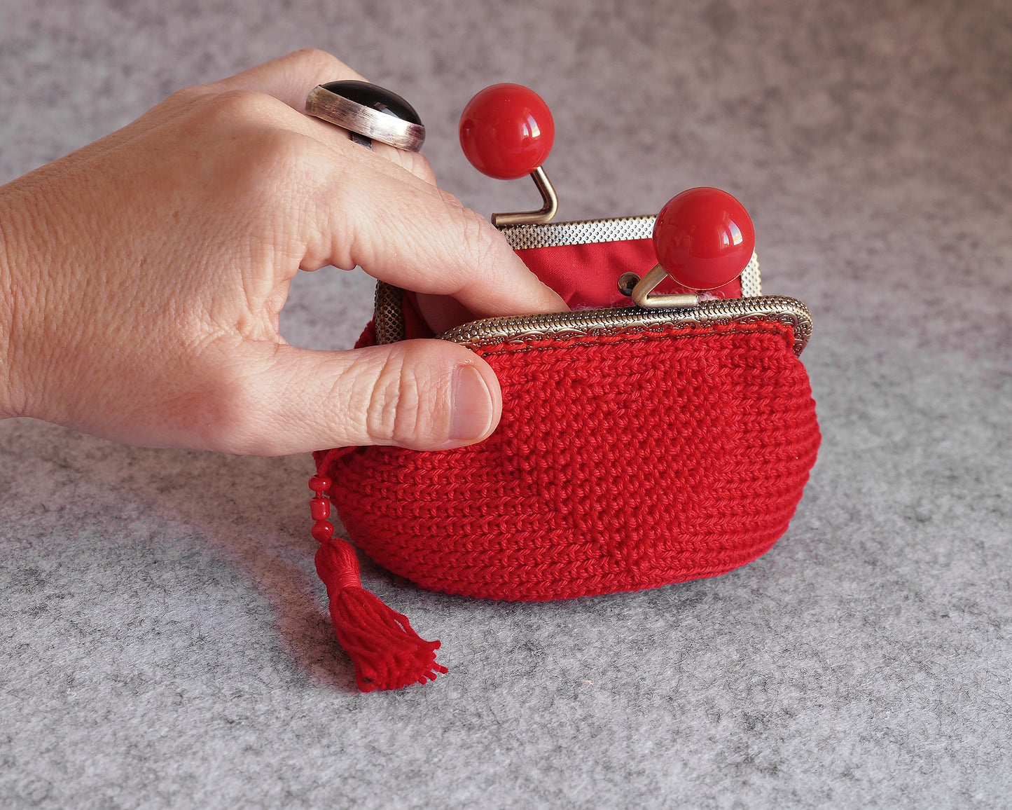 mano guardando algo en un monedero de ganchillo rojo con cierre de boquilla bolas rojas