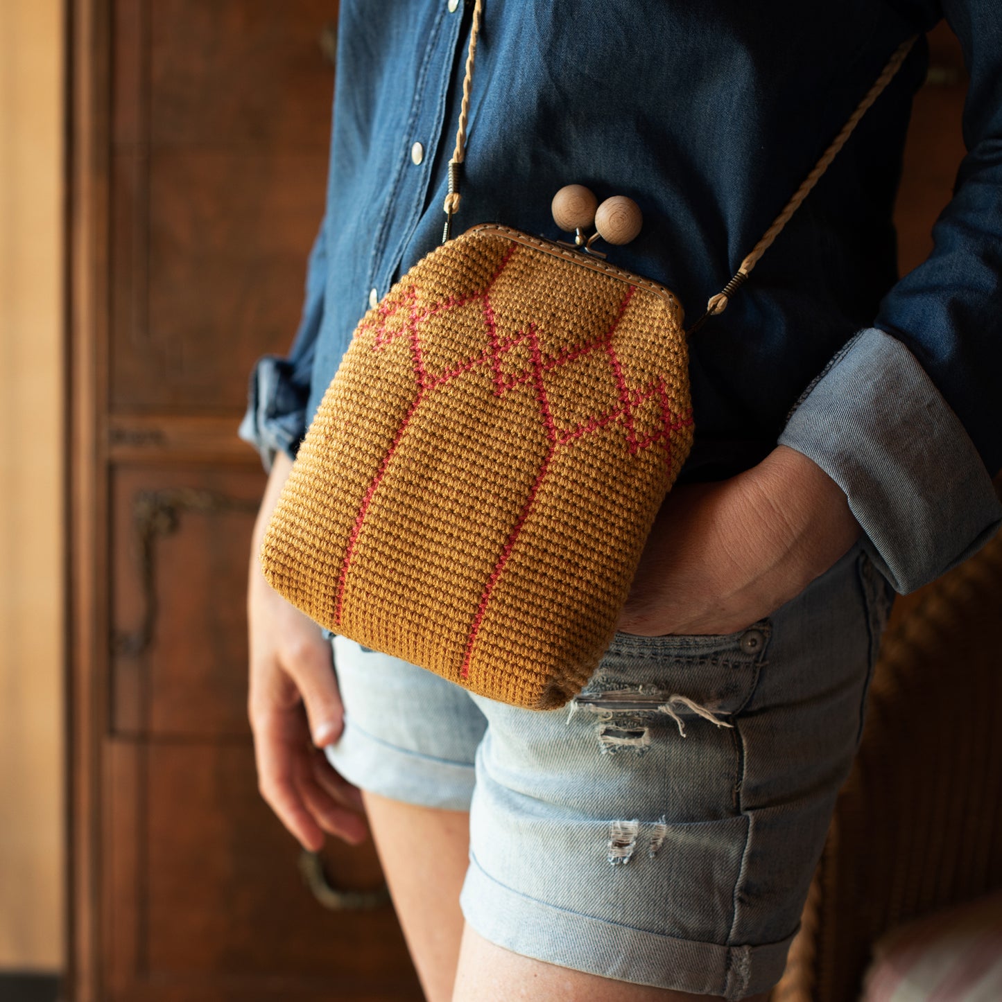 mujer que lleva un bolso pequeño de ganchillo con boquilla de bolas de madera y correa trenzada color beige