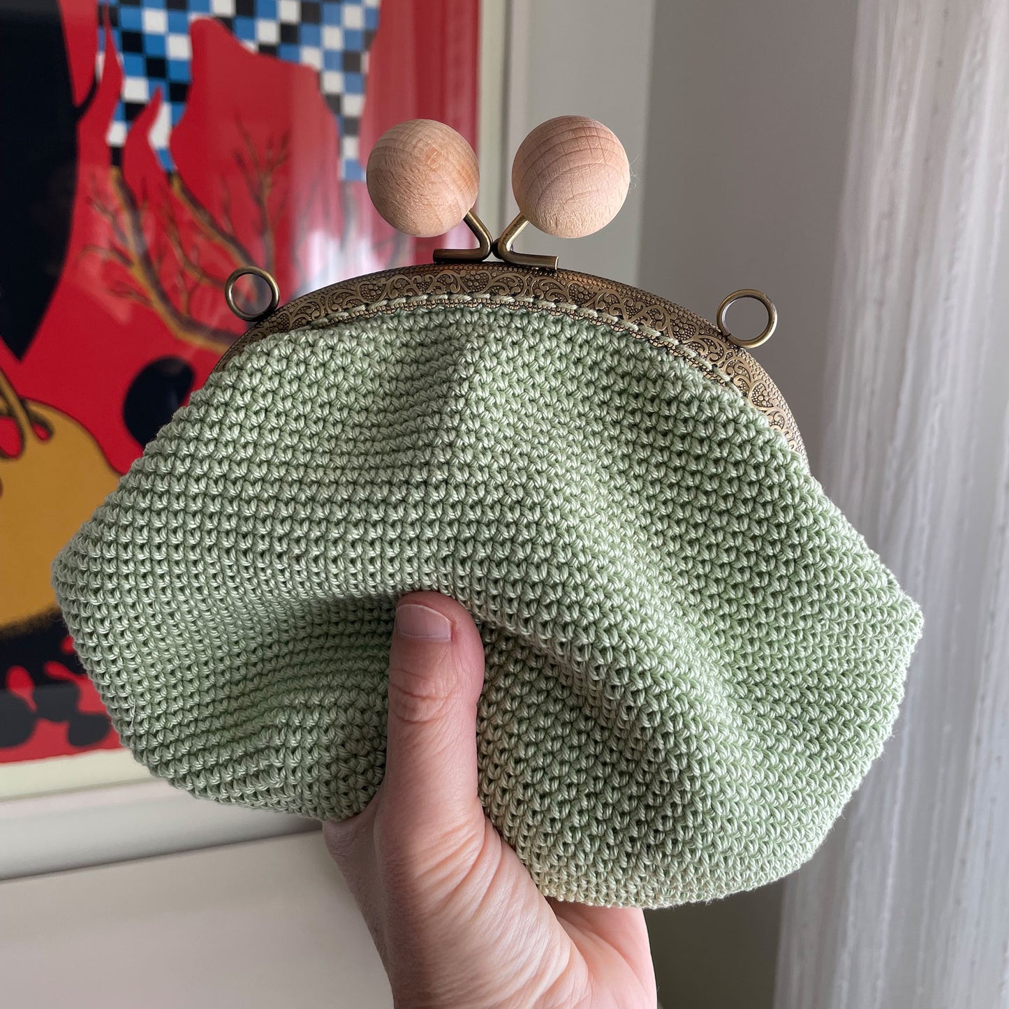 Bolso de mano de crochet en color verde salvia con cierre de boquilla redonda y grandes bolas de madera natural