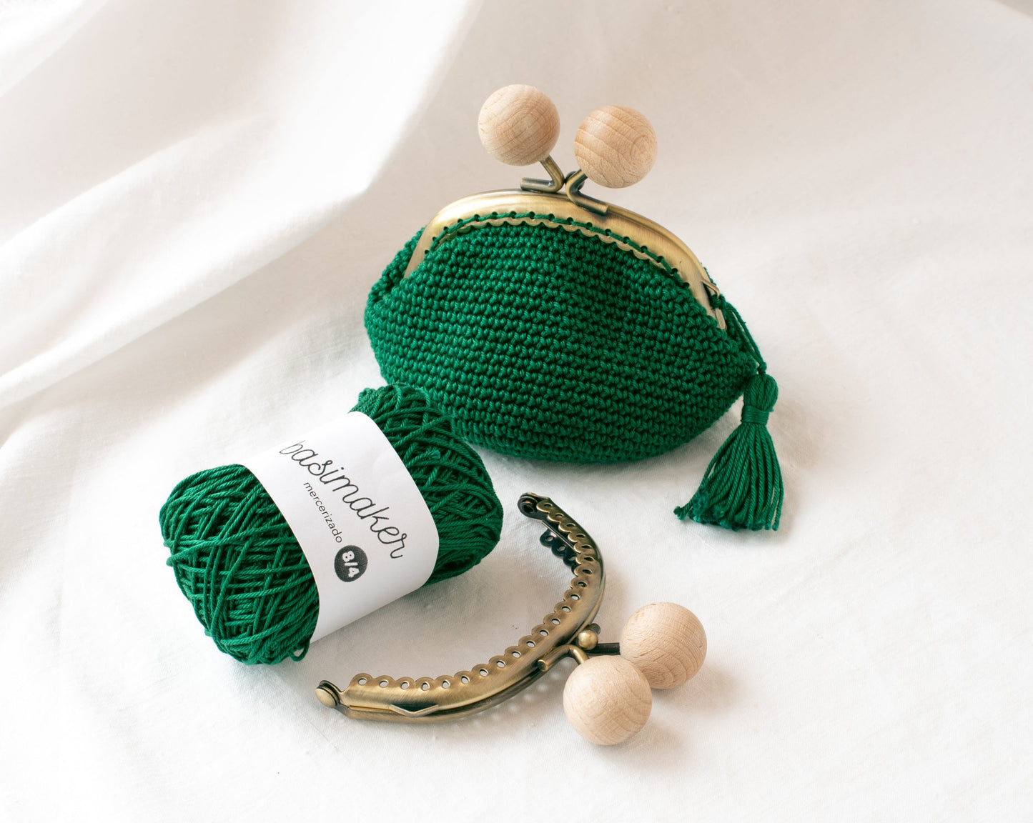 Monedero de crochet verde oscuro hecho a crochet, con ovillo verde y boquilla redonda metálica y bolas de madera