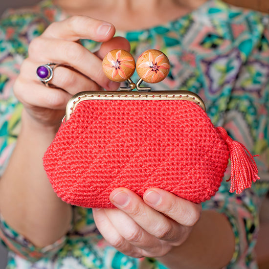 mujer sujeta en su mano un monedero de crochet tejido por ella en color coral y bolas de madera pintadas a mano con flores