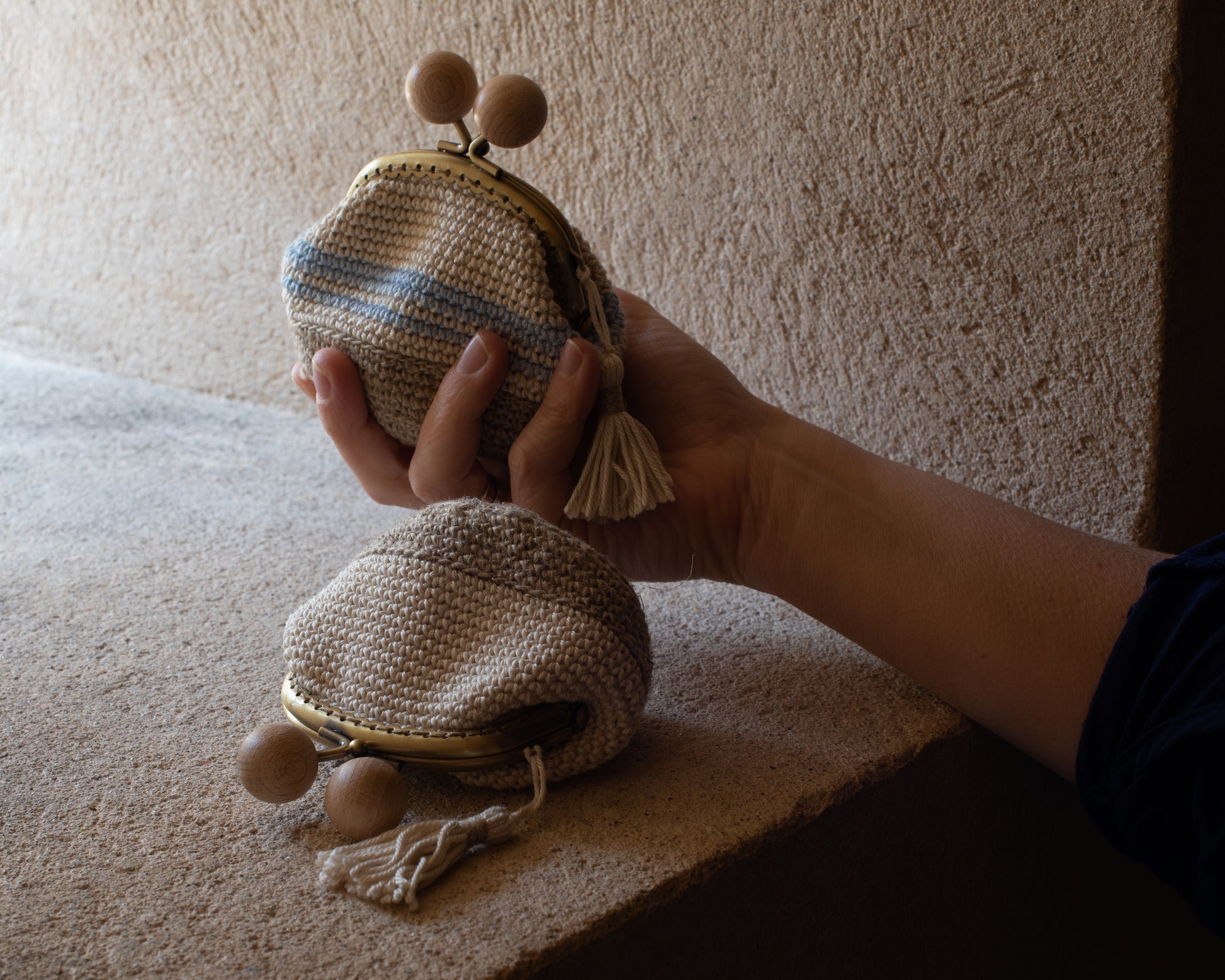 mano de mujer sujeta un monedero de crochet junto a otro monedero de estilo rústico en una ventana