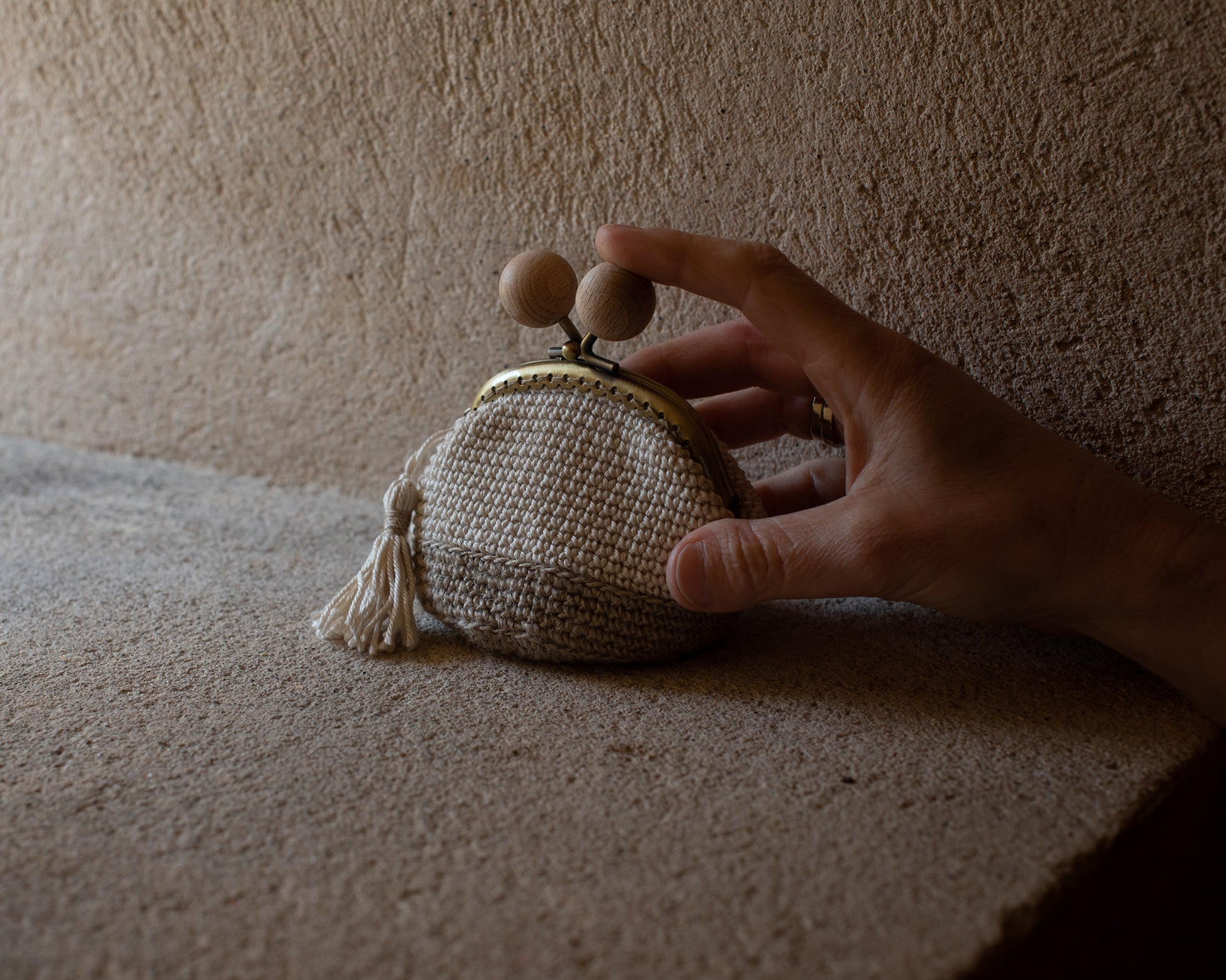 mano sujeta un monedero tejido a mano en crochet en tonos naturales de lino y algodón