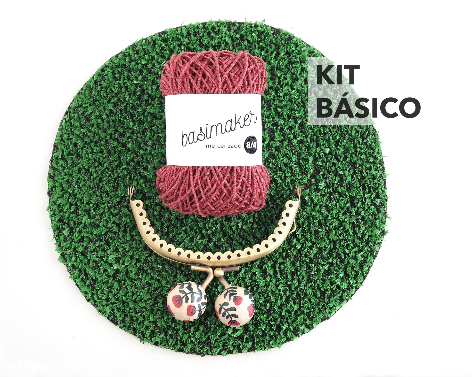 kit básico compuesto por ovillo de hilo rojo y boquilla para monedero sobre círculo de cesped artificial